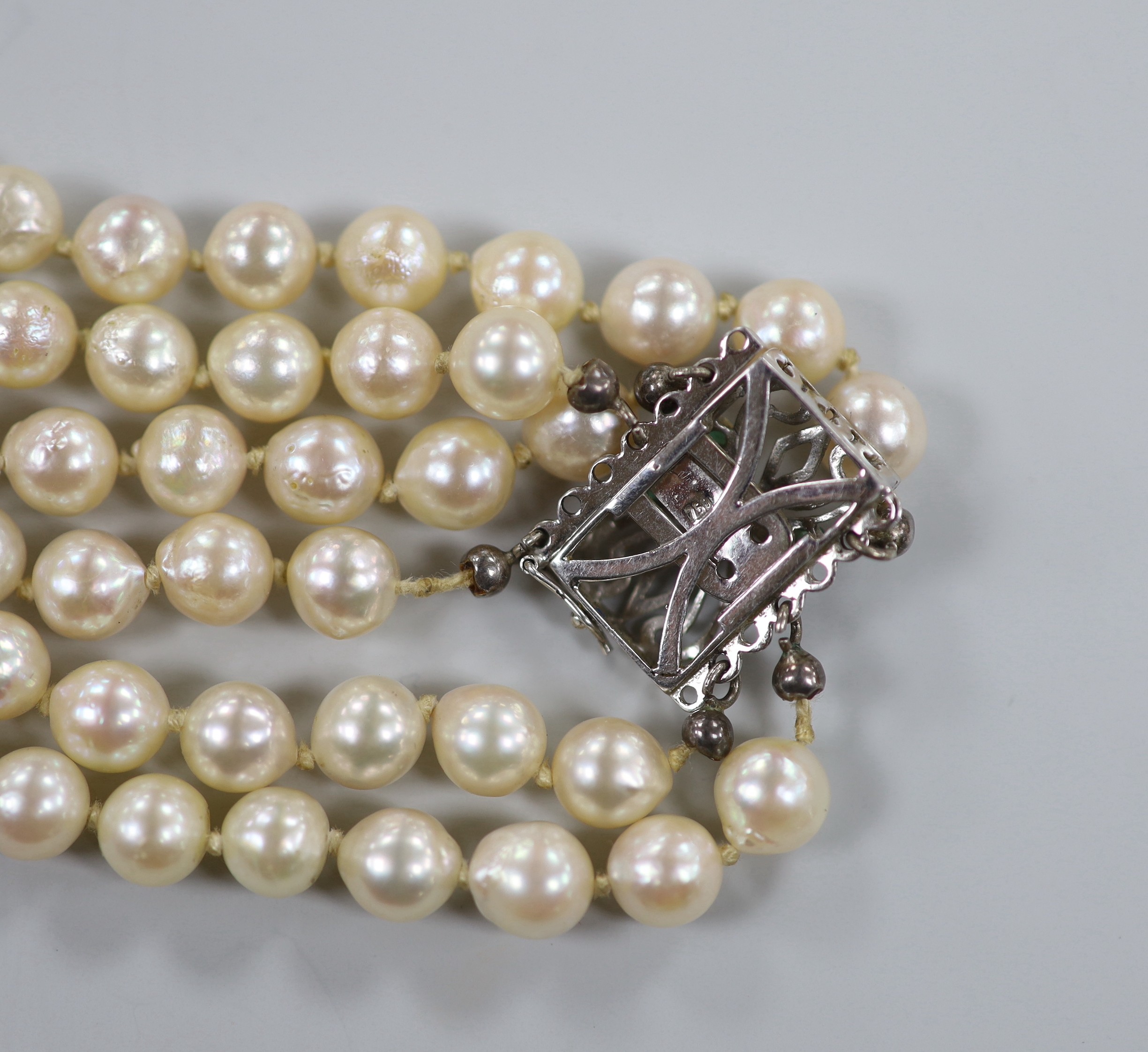 A mid to late 20th century triple strand cultured pearl necklace, with pierced 750 white metal and five stone emerald chip set clasp, approximately 56cm.